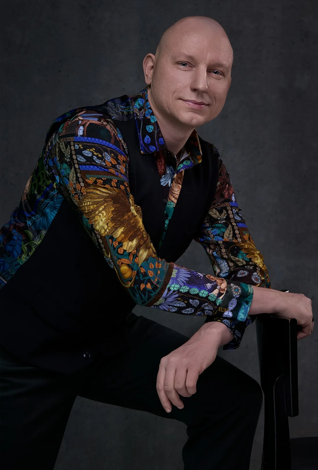 Dariusz Chęciński-Kamiński w kolorowej koszuli, oparty o krzesło
